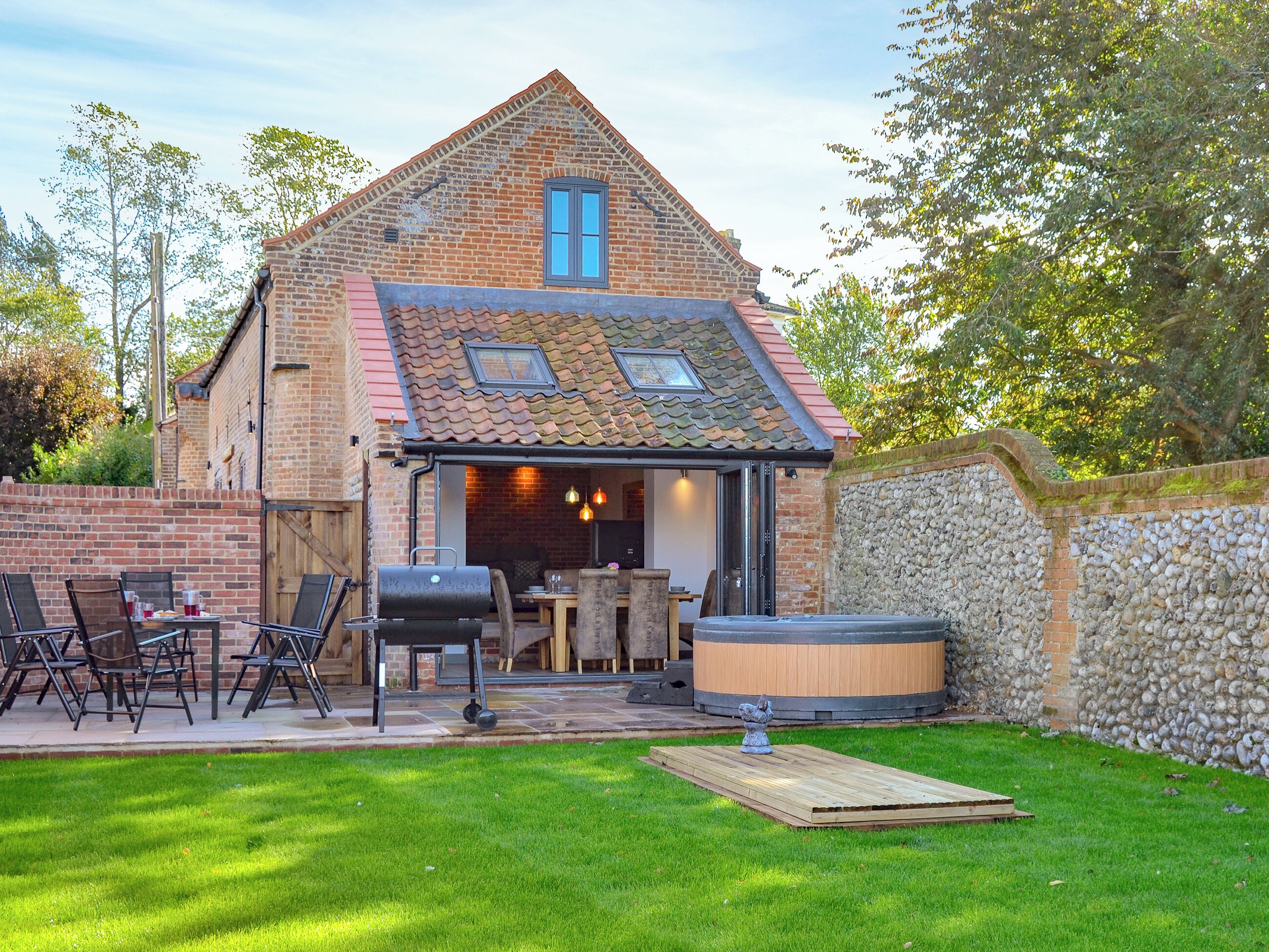 Une maison en briques avec un toit en tuiles, une terrasse avec des meubles d’extérieur, un jacuzzi et un mur en pierre.