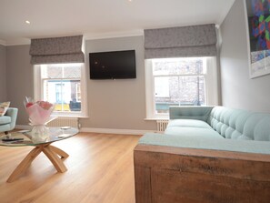 A living room with a light blue sofa, a glass coffee table, and a bouquet of flowers. - 3 bedroom accommodation in York (York)