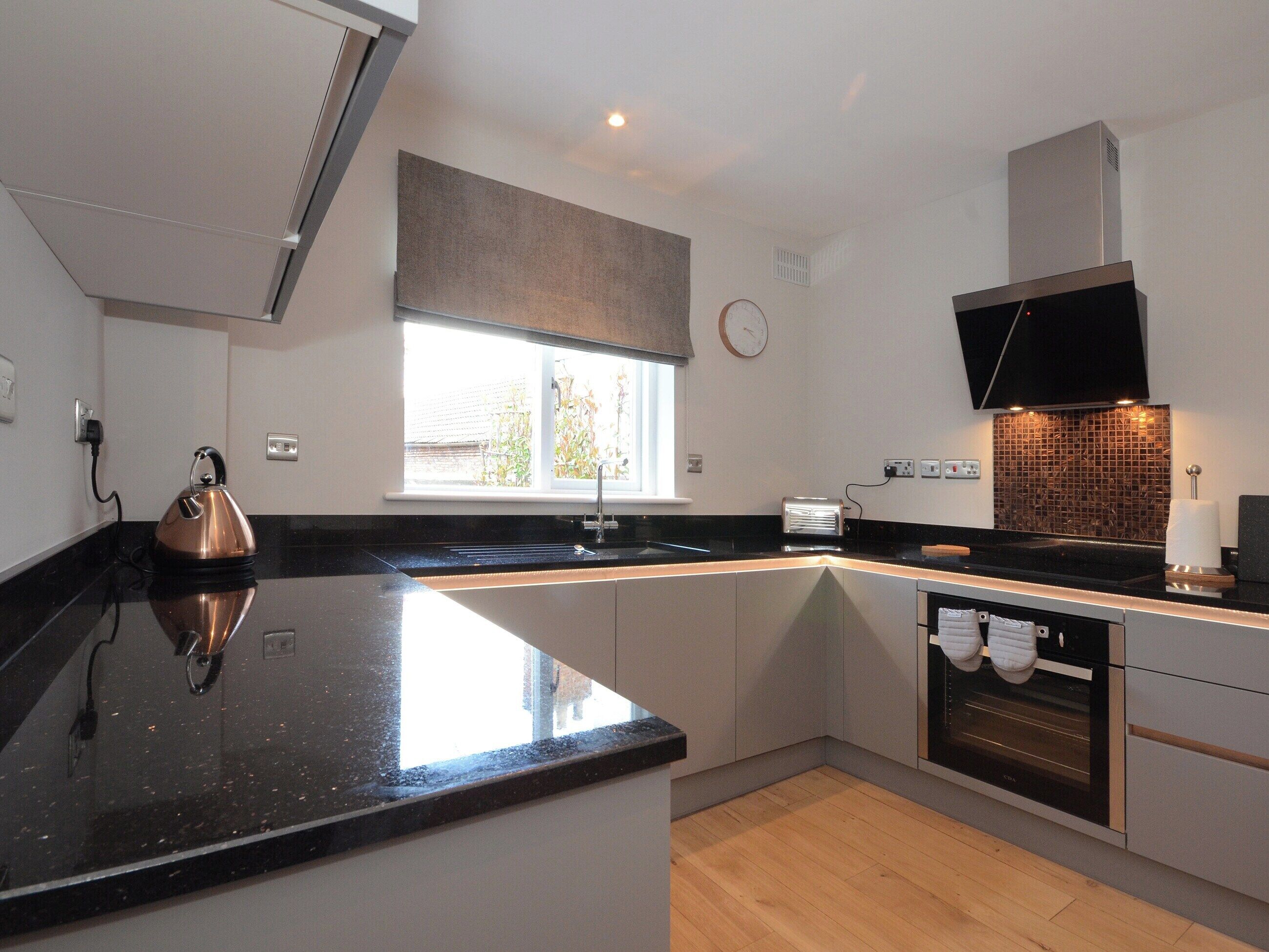 A modern kitchen with a black countertop, stainless steel appliances, a window with a view, and a clock on the wall.