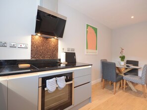 A modern kitchen with a built-in oven, a microwave, and a gas stove. There is a dining area with a table and chairs, and a potted plant on the table. - 3 bedroom accommodation in York (York)