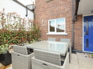 A patio area with a glass-top table and wicker chairs, a brick wall, and a blue door. - 3 bedroom accommodation in York (York)