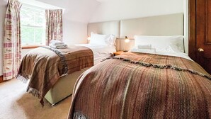 Ein Hotelzimmer mit zwei Betten, einem Fenster mit Vorhängen, einem Nachttisch mit Lampe und einer Tür.