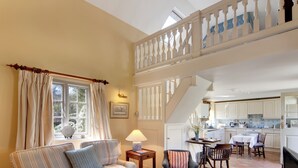 A living room with a sofa, armchair, coffee table, and a staircase leading to a kitchen. - 1 bedroom accommodation in Bruern, near Chipping Norton (Bruern, near Chipping Norton)