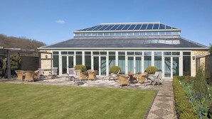 A building with a large glass facade, a sloped roof with solar panels, and an outdoor patio with wicker furniture. - 1 bedroom accommodation in Bruern, near Chipping Norton (Bruern, near Chipping Norton)