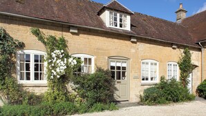 A stone building with a tiled roof, multiple windows, and a gravel driveway. - 1 bedroom accommodation in Bruern, near Chipping Norton (Bruern, near Chipping Norton)