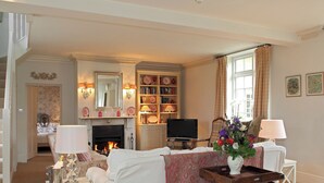 Een woonkamer met een open haard, een televisie, een boekenkast en een eethoek met een tafel en stoelen.