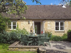 A stone house with a tiled roof, a garden with green chairs and a table, and a window with flowers. - 3 bedroom accommodation in Bruern, near Chipping Norton (Bruern, near Chipping Norton)
