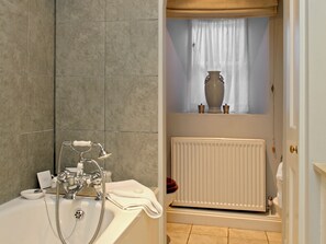 A bathroom with a bathtub, a shower, a radiator, and a window with a vase. - 3 bedroom accommodation in Bruern, near Chipping Norton (Bruern, near Chipping Norton)