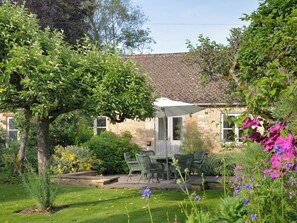 A stone house with a patio, green chairs, and a table. - 3 bedroom accommodation in Bruern, near Chipping Norton (Bruern, near Chipping Norton)