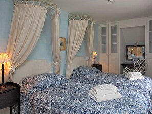 Ein Schlafzimmer mit Himmelbett, zwei Nachttischen, einem Sessel, einem Kleiderschrank und einem Spiegel.