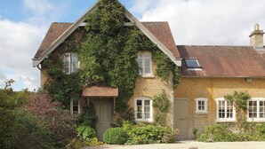 Une maison en pierre avec un toit en pente, une petite dépendance attenante et une allée gravillonnée.