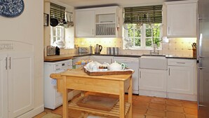 A kitchen with white cabinets, a wooden table, a dish rack, and a window with blinds. - 3 bedroom accommodation in Bruern, near Chipping Norton (Bruern, near Chipping Norton)