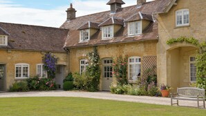 A stone building with multiple windows, a gravel driveway, and a grassy lawn. - 3 bedroom accommodation in Bruern, near Chipping Norton (Bruern, near Chipping Norton)