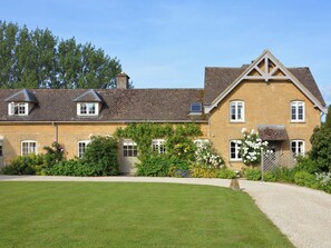 Ein traditionelles Steinhaus mit gepflegtem Rasen, einem Kiesweg und verschiedenen blühenden Pflanzen.