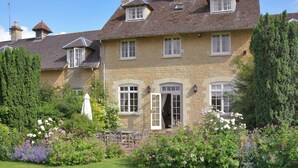 A stone building with multiple windows and a door, surrounded by a well-maintained garden with various flowers and a lawn. - This truly unique property will appeal to guests looking for a touch of luxury. (Bruern, near Chipping Norton)