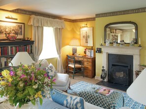 A cozy living room with a fireplace, a bookshelf, a desk with a lamp, and a comfortable seating area. - Cheltenham - UKC1155 (Bruern, near Chipping Norton)