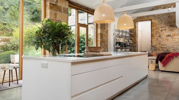 A modern kitchen with a large island, stone walls, and large windows offering a view of greenery. - 4 bedroom accommodation in Longframlington, near Rothbury (Longframlington, near Rothbury)