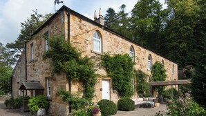 A stone building with a sloped roof, a satellite dish, and a covered patio area with outdoor seating. - 4 bedroom accommodation in Longframlington, near Rothbury (Longframlington, near Rothbury)