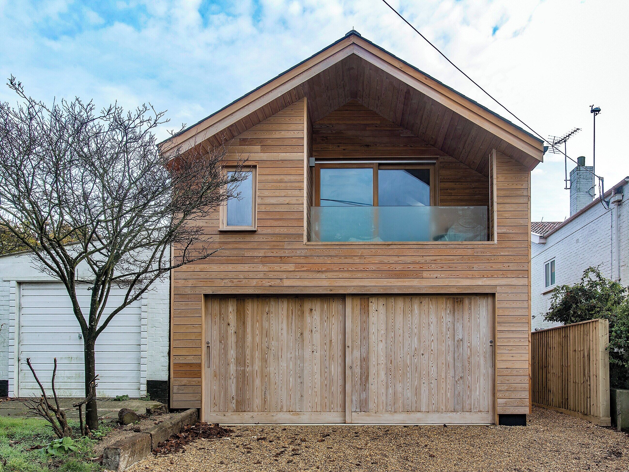 Ein zweigeschossiges Holzhaus mit Garage, einem kleinen Fenster im Obergeschoss und einem Baum im Vordergrund.