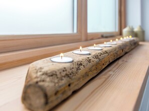 Kerzenreihe auf einem Holzstamm, platziert auf einem Fensterbrett.