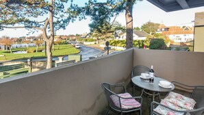 Een balkon met een tafel en stoelen, met uitzicht op een straat en groen.
