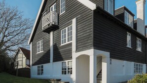 Ein zweigeschossiges Haus mit einem steilen Dach, weißem Zierdekor und einem kleinen Balkon mit Geländer.
