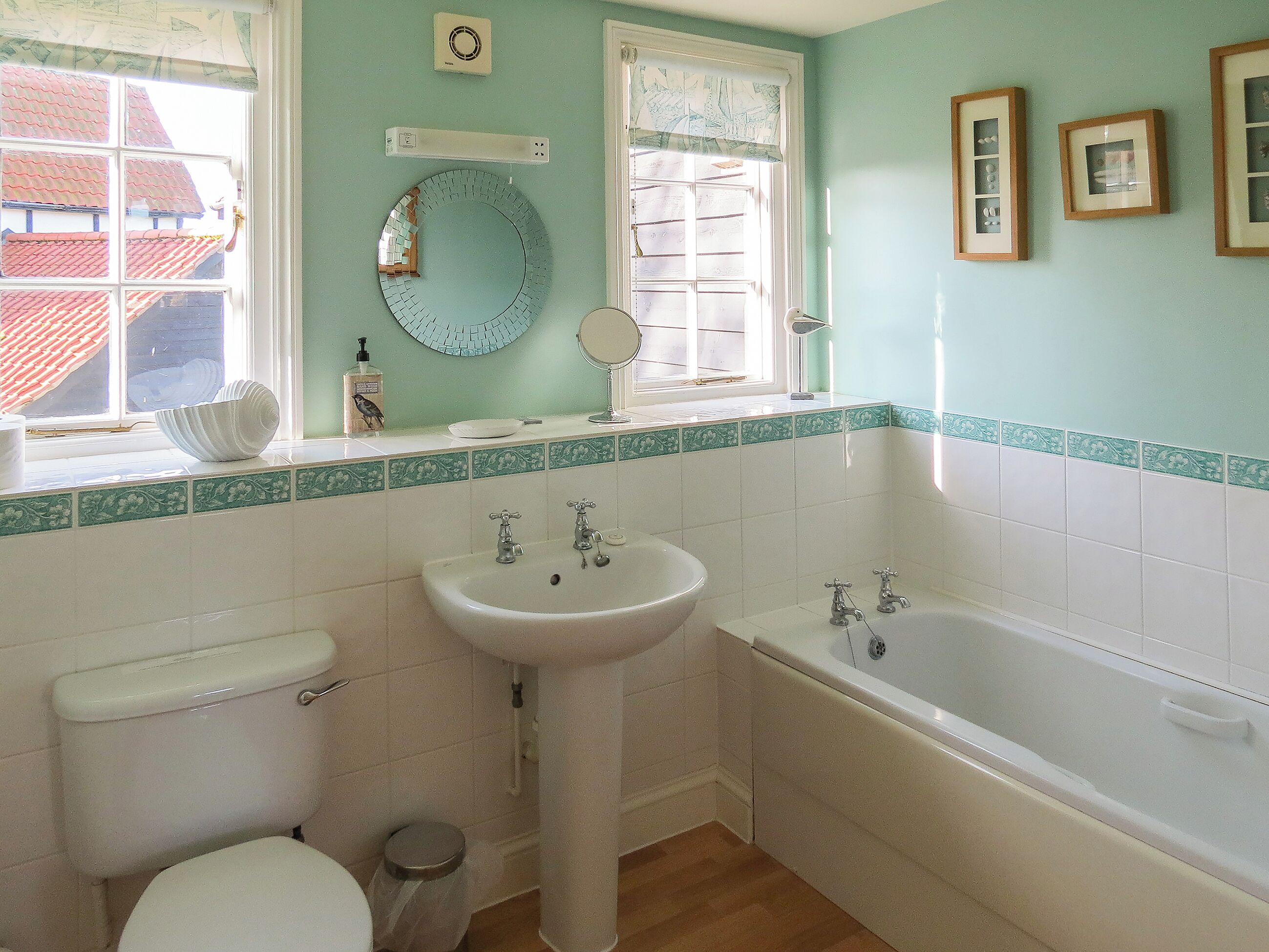 A bathroom with a toilet, sink, and bathtub. There is a window with a view of a red-roofed building outside.