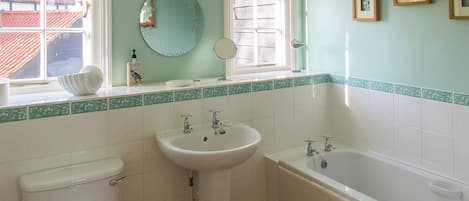 A bathroom with a toilet, sink, and bathtub. There is a window with a view of a red-roofed building outside.