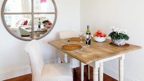 A dining area with a wooden table, white chairs, a mirror, a bowl of fruit, a bottle of wine, and a potted plant. - 1 bedroom accommodation in Thorpeness, near Aldeburgh (Thorpeness, near Aldeburgh)