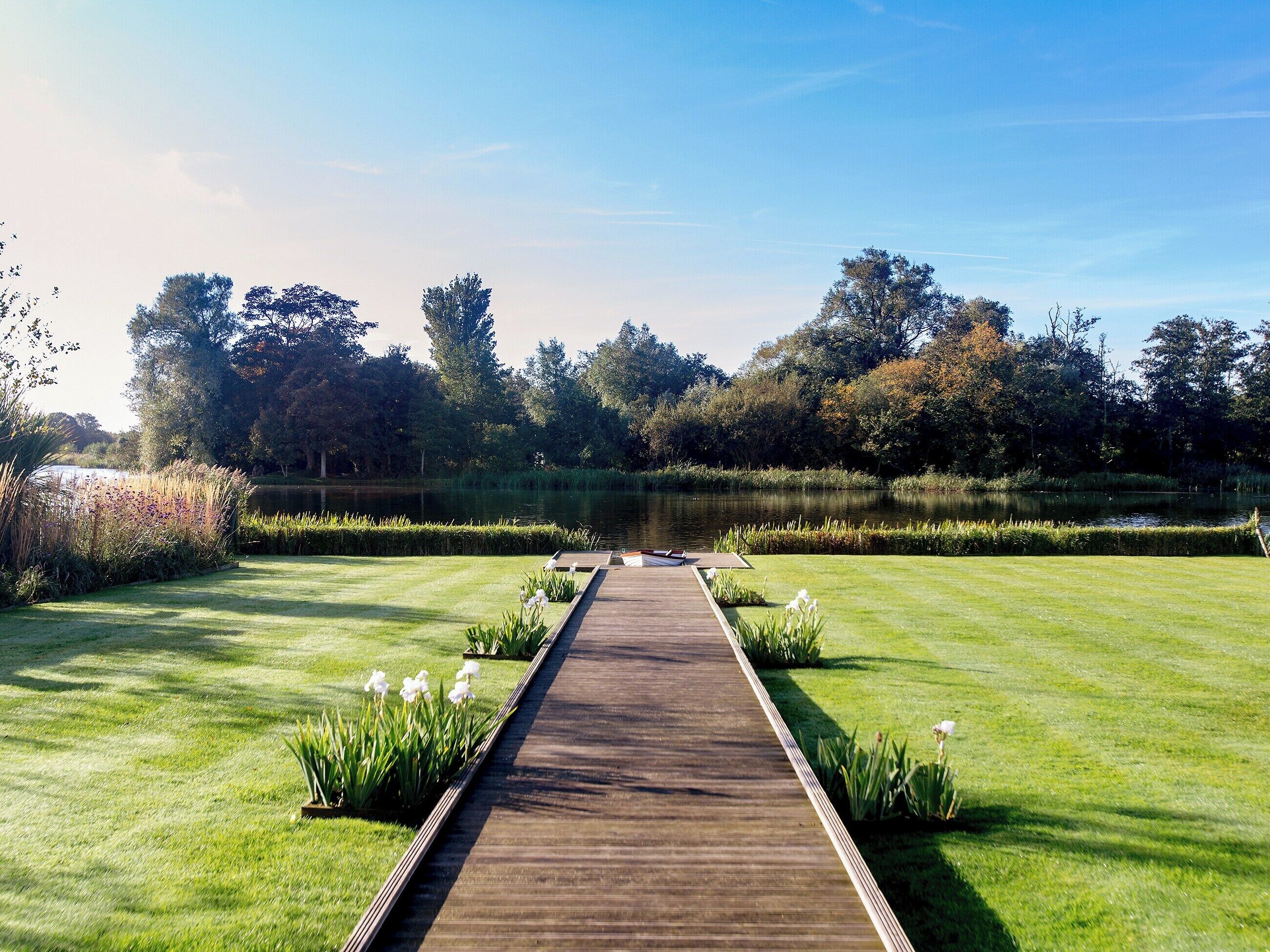 A wooden pathway leading to a pond, surrounded by well-maintained grass and trees.