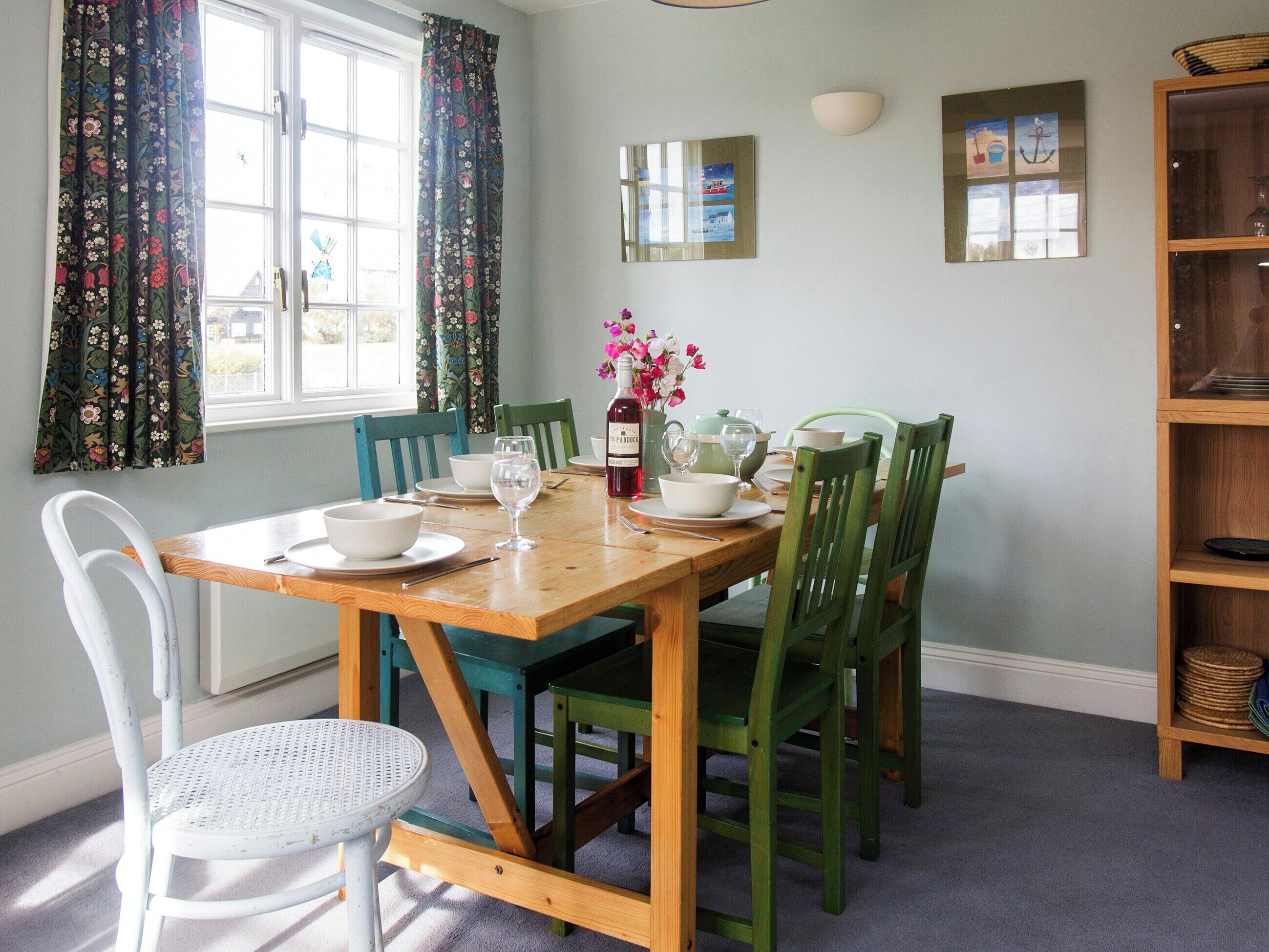 A dining room with a wooden table set for four, green chairs, a white chair, and a small round table.