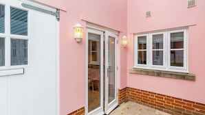 Eine rosa Außenwand mit einer weißen Tür und Fenstern, einer Ziegelbasis und einer mit Herbstlaub bedeckten Pflasterterrasse.