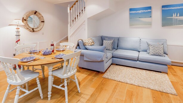 Ein modernes Wohnzimmer mit einem Holzespeisetisch, gedeckt für vier Personen, einem hellblauen Sofa, weißen Stühlen, einer Treppe und Meereskunst.