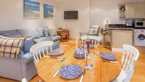 Ein modernes Wohnzimmer mit einem blauen Sofa, einem Esstisch für vier Personen und einer Küchenzeile mit Geräten.
