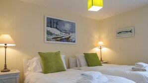 Een hotelkamer met twee bedden, elk voorzien van witte lakens en groene kussens. Twee bedlampen, een schilderij aan de muur, en een lijst met een foto boven het bed.