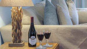 Een kamer met een bank, een lamp, een fles wijn en twee wijnglazen op een houten bijzettafeltje.