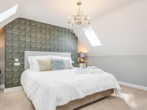 Ein Schlafzimmer mit einem gebogenem Kopfteil, einer Chandelieber, einem Bett mit weißer Bettwäsche und einem Nachttisch mit einer Lampe.