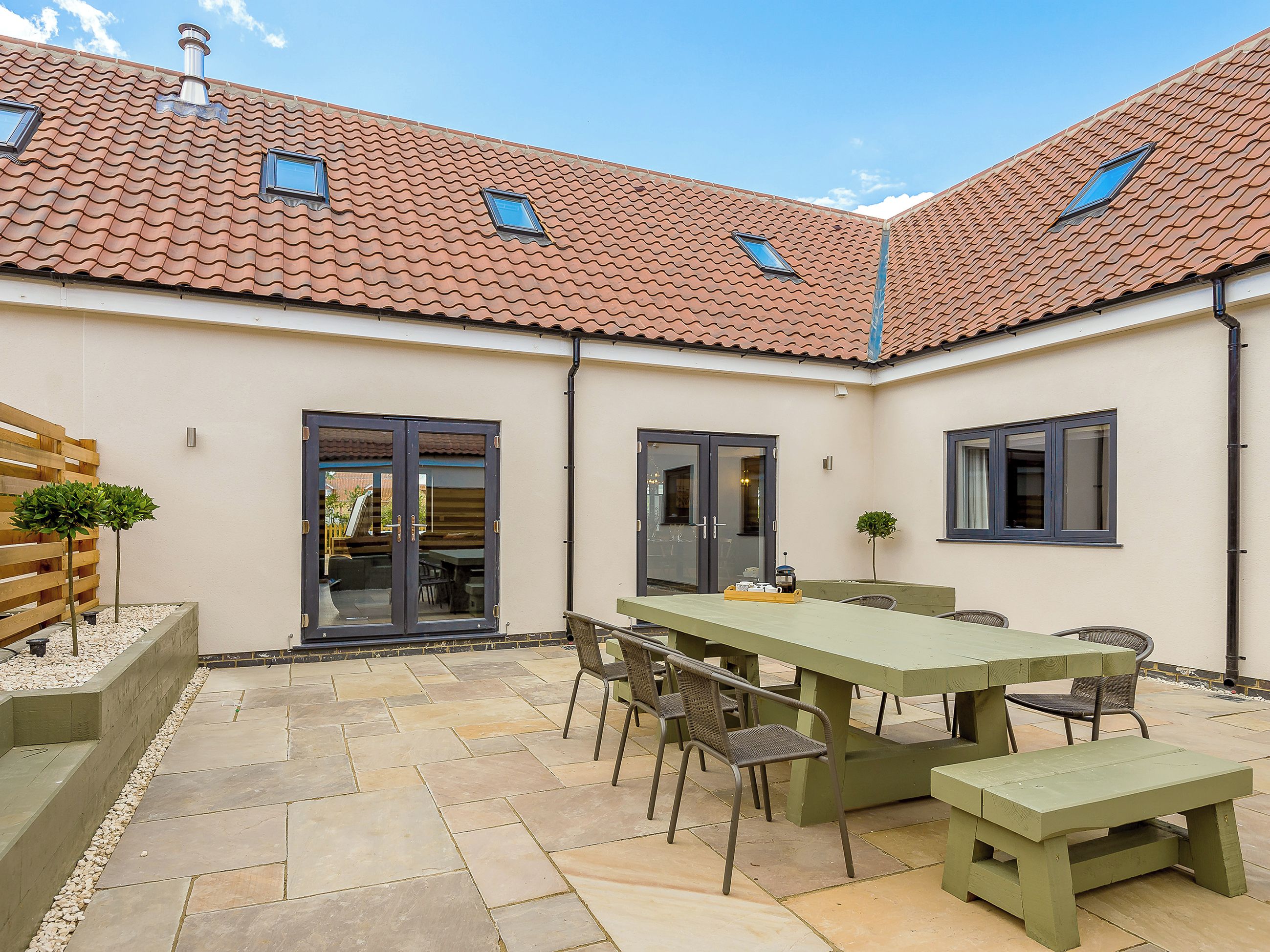 A courtyard with a tiled roof, a dining table with chairs, and a bench.