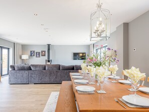 Ein moderner Essbereich mit einem Holztisch, gedeckt für vier Personen, einem grauen Sofa im Hintergrund und einer Chandelüstere darüber.