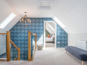 A bedroom with a sloped ceiling, a chandelier, a bed, a bench, and a staircase with glass railings. - 5 bedroom accommodation in Dunholme, near Lincoln (Dunholme, near Lincoln)