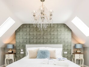 Ein Schlafzimmer mit einem gebügelten Kopfteil, einer Chandelierleuchtre, zwei Nachttischen mit Lampen sowie einem Bett mit Kissen und Decke.