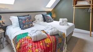 Une chambre à coucher avec un lit, des oreillers, une couverture colorée, une étagère en bois avec des serviettes et des fenêtres de toit.