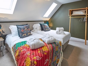 Ein Schlafzimmer mit Bett, Kissen, einer bunten Decke, einem hölzernen Regal mit Handtüchern und Dachfenstern.