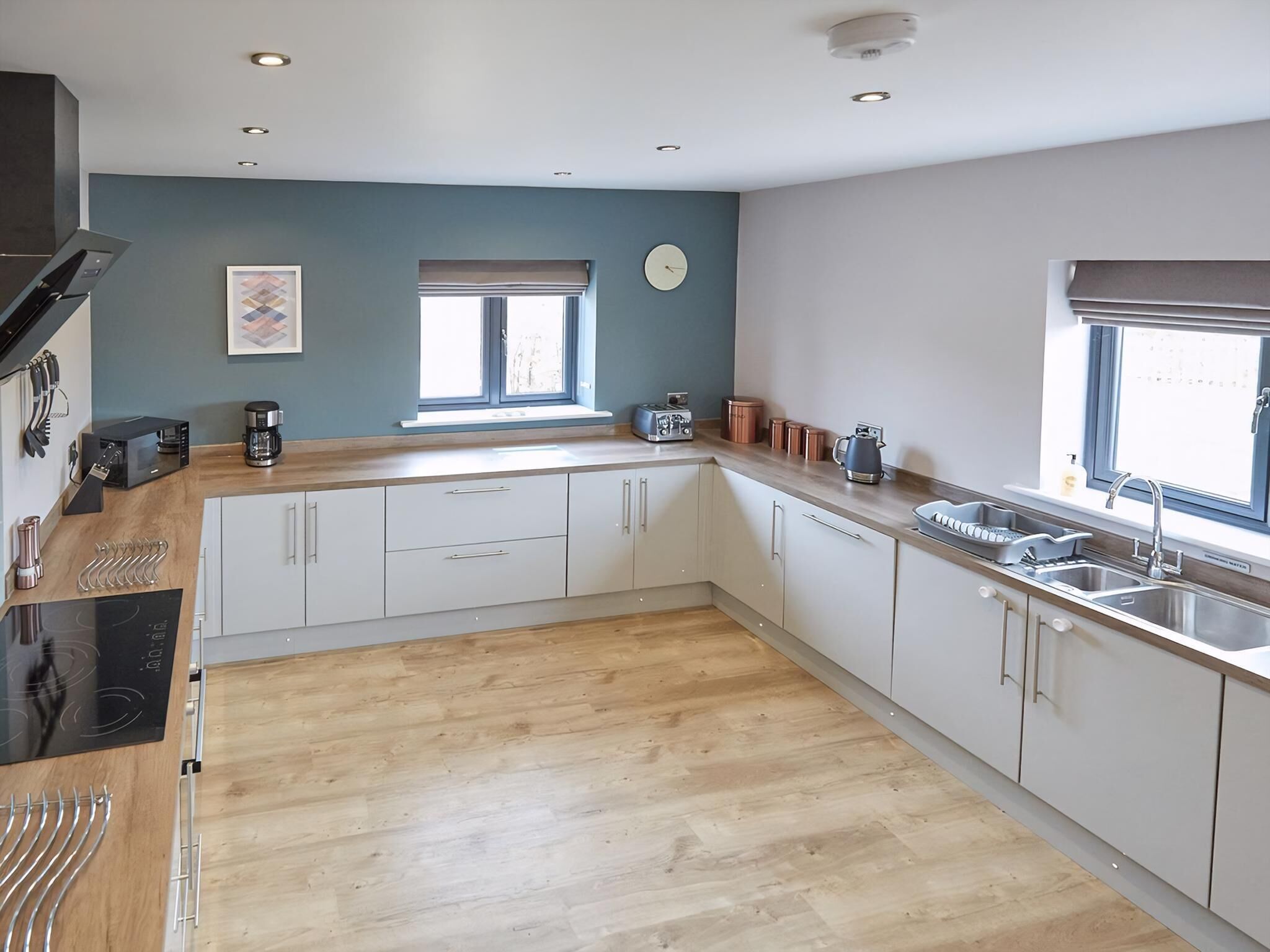 A modern kitchen with wooden flooring, white cabinets, a built-in oven, and a window with blinds.