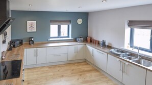 Une cuisine moderne avec un plancher en bois, des armoires blanches, un four encastré et une fenêtre avec des stores.