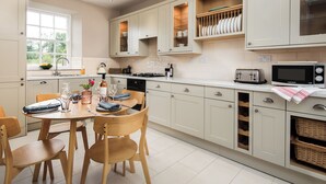 A modern kitchen with white cabinetry, a dining table with chairs, and a window providing natural light. - 2 bedroom accommodation in Longframlington, near Rothbury (Longframlington, near Rothbury)