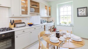 A modern kitchen with white cabinets, a gas stove, a microwave, and a dining table set for four. - 2 bedroom accommodation in Longframlington, near Rothbury (Longframlington, near Rothbury)