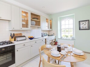 A modern kitchen with white cabinets, a gas stove, a microwave, and a dining table set for four. - 2 bedroom accommodation in Longframlington, near Rothbury (Longframlington, near Rothbury)