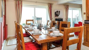Comedor con mesa de madera preparada para cuatro, rodeada de sillas y vista a zonas verdes.