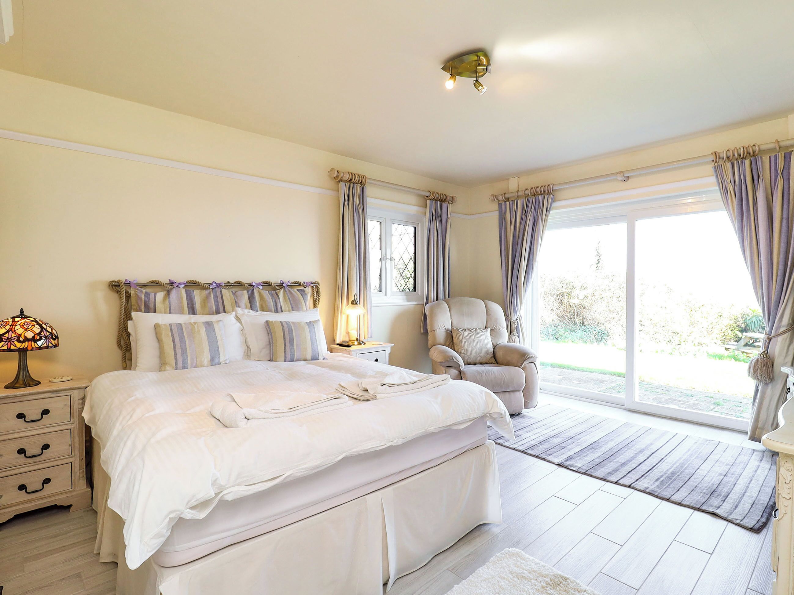 Ein Schlafzimmer mit Bett, Nachttisch, Lampe, Stuhl und Blick ins Freie.